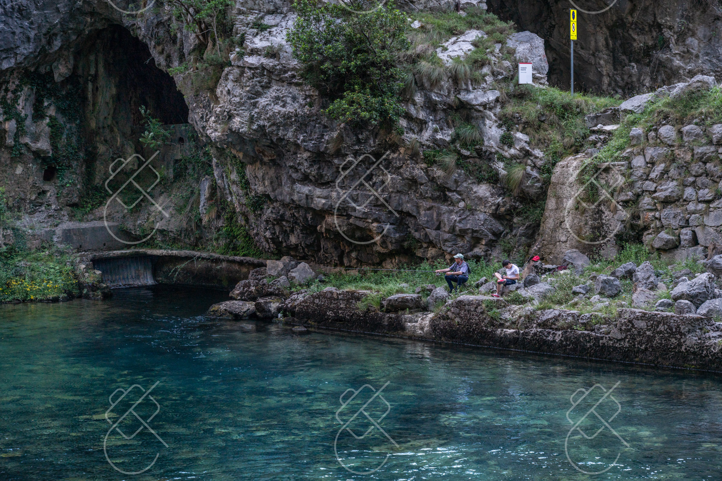 Turquoise water running beneath a limestone cliff wall in the Cares Gorge — Poncebos