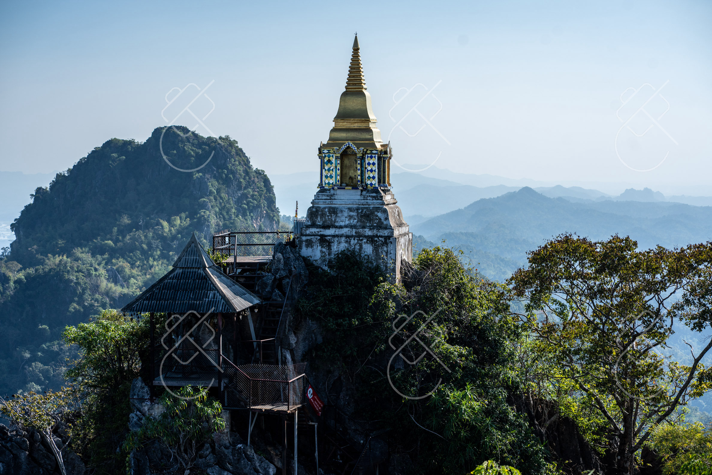 A golden stupa on a rocky forested peak above Lampang — Lampang