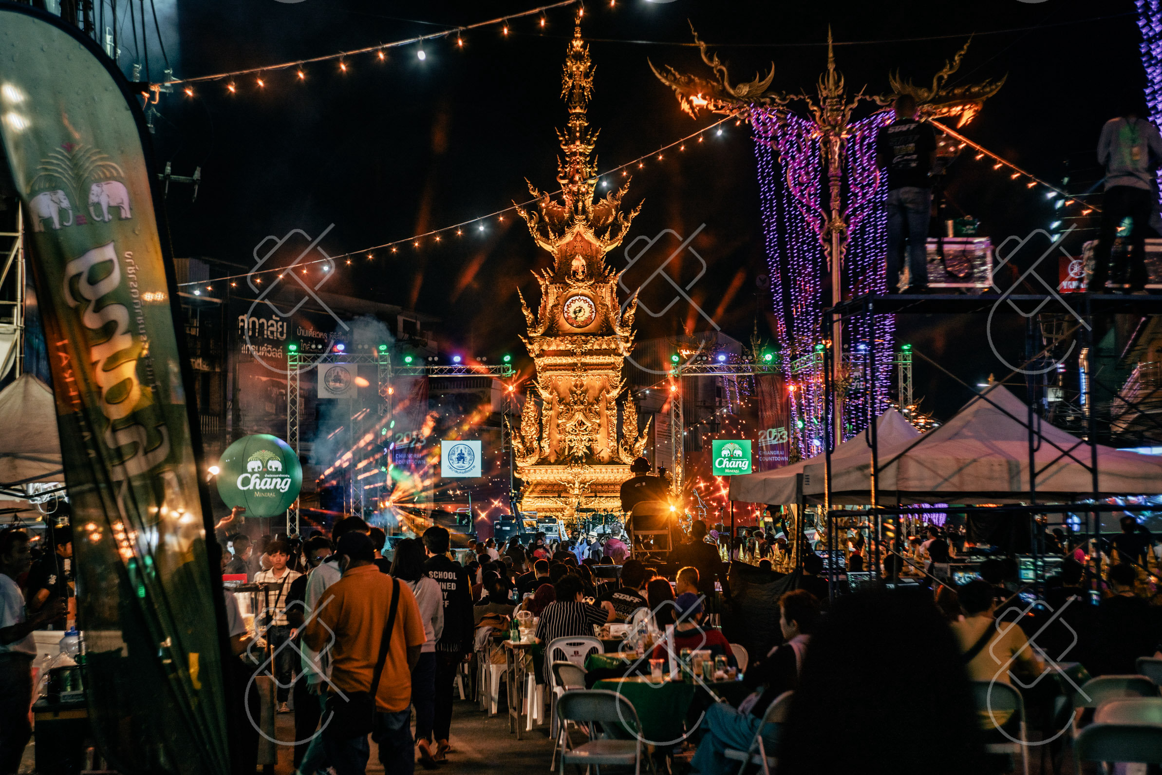 Chiang Rai's gilded clock tower lit up behind a crowded night of street stalls and string lights — Chiang Rai, fine art travel photography print available from Clever Tourists