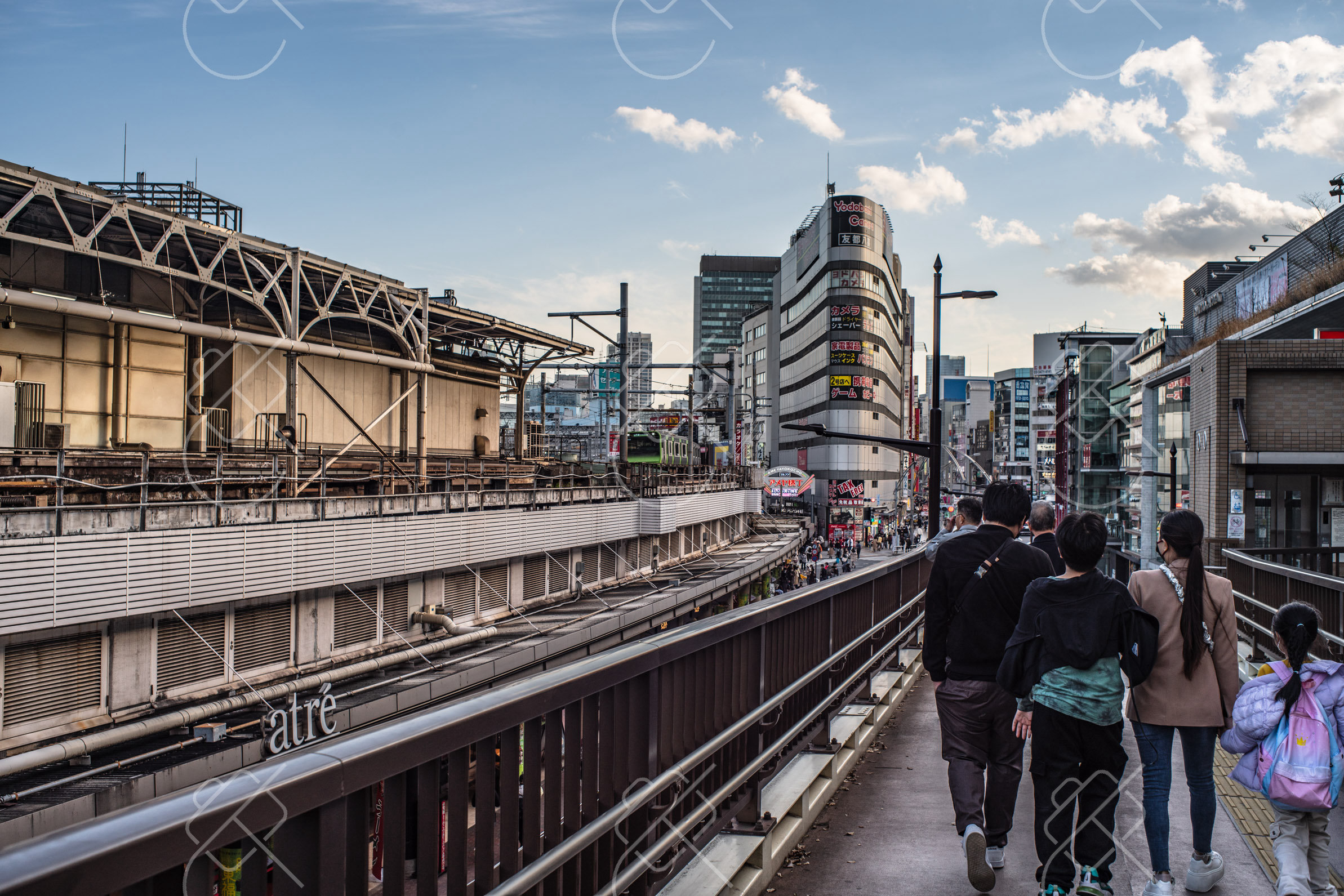A footbridge over the JR tracks in Tokyo, where one tap of a phone Suica covers the train, the station shops and the vending machines
