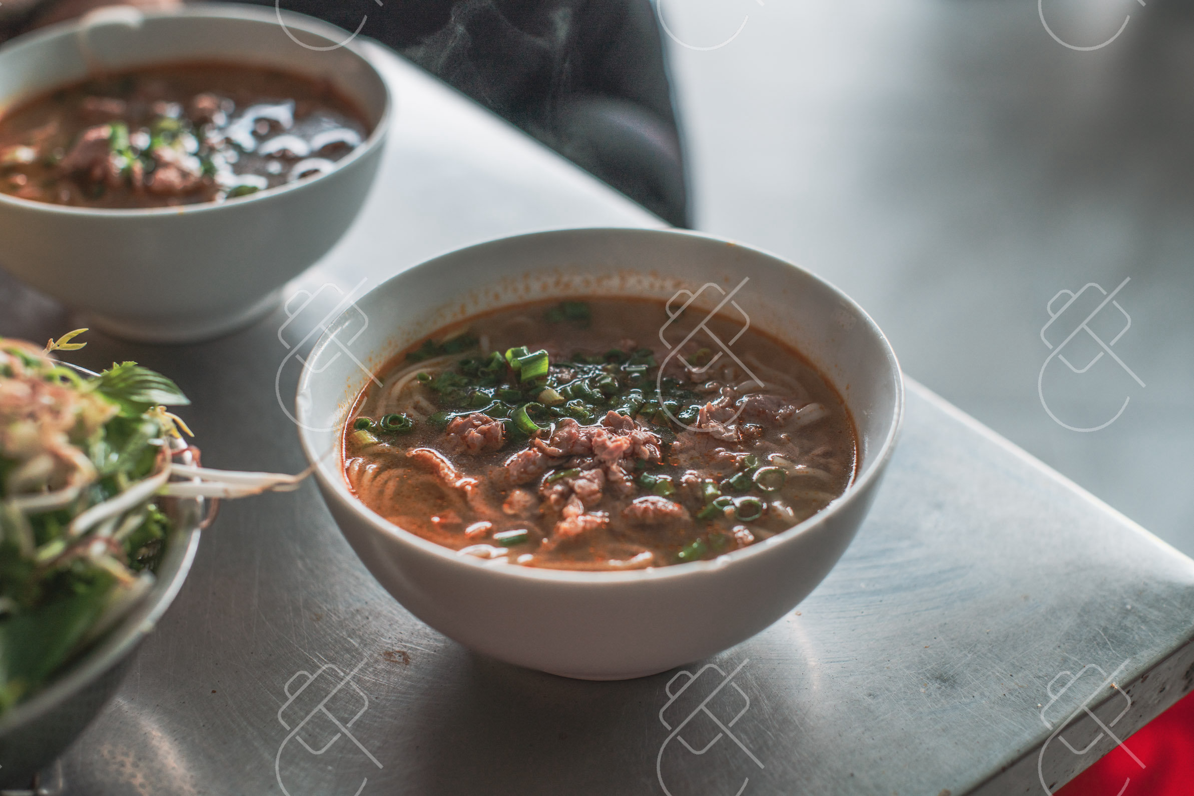 Bowls of bun bo Hue with a plate of fresh herbs on the side — Hue, fine art travel photography print available from Clever Tourists