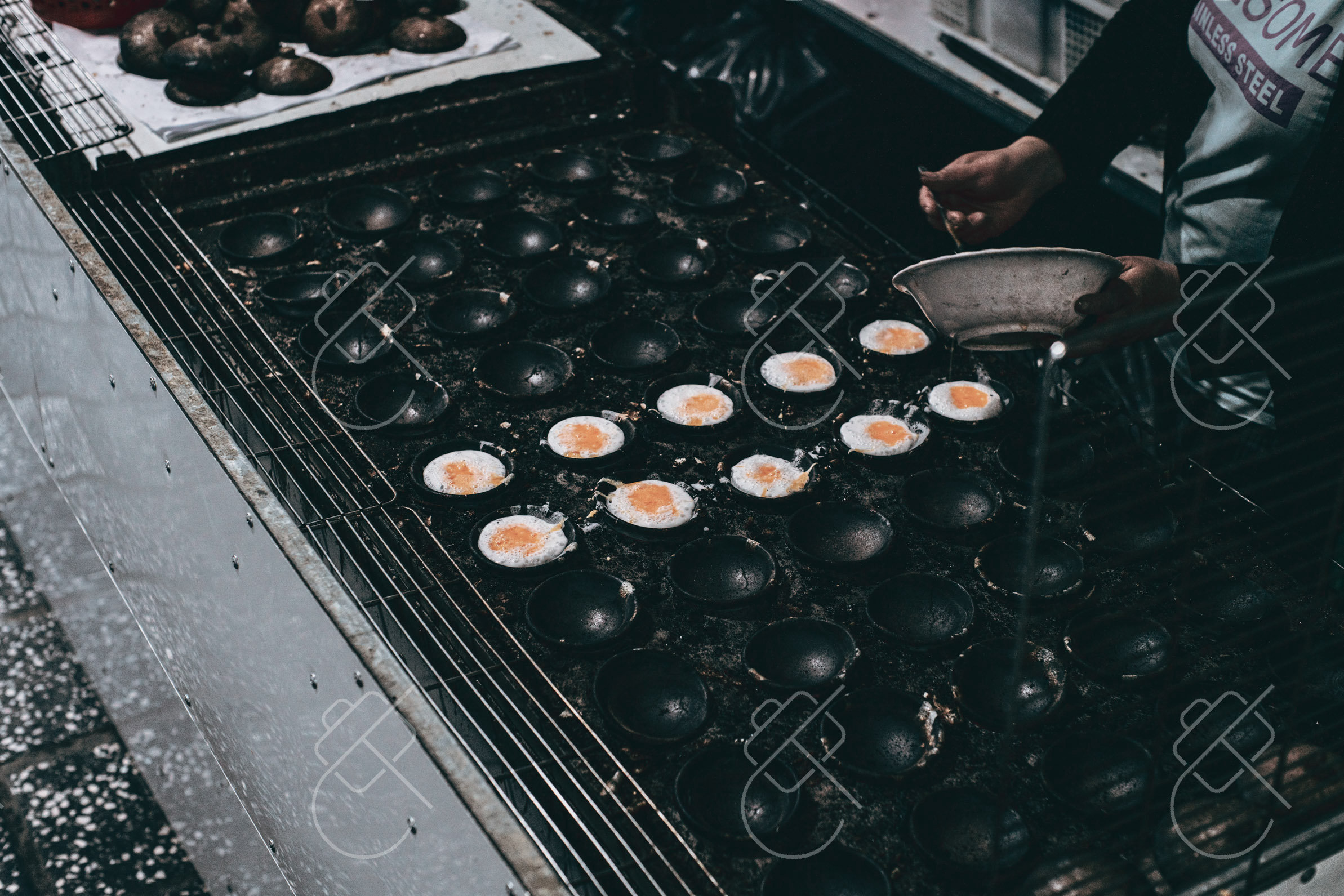 Banh can batter sizzling in rows of round molds on a street griddle — Da Lat, fine art travel photography print available from Clever Tourists