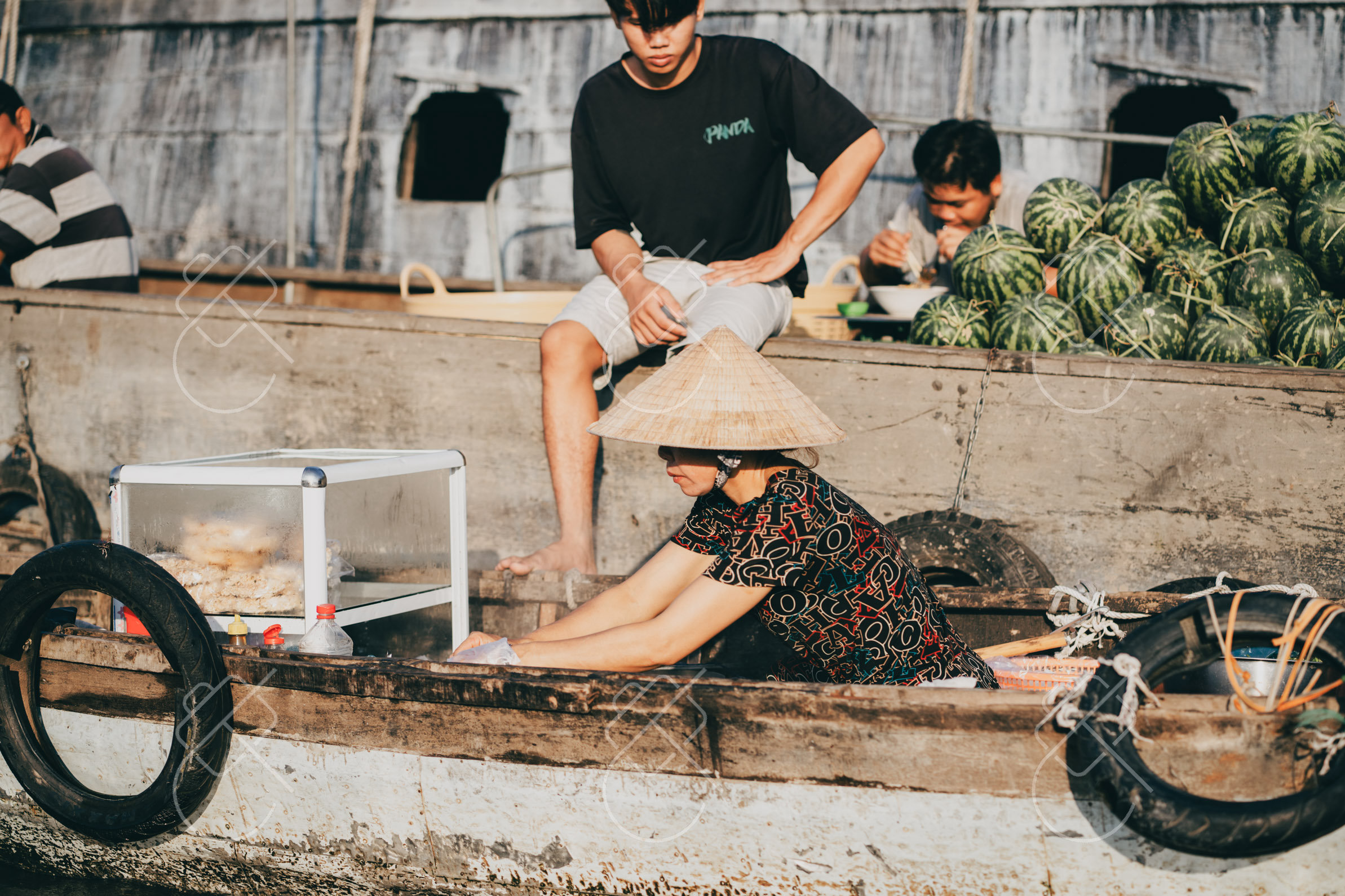 Vendor cooking breakfast on her boat with watermelons stacked behind her — Can Tho, fine art travel photography print available from Clever Tourists